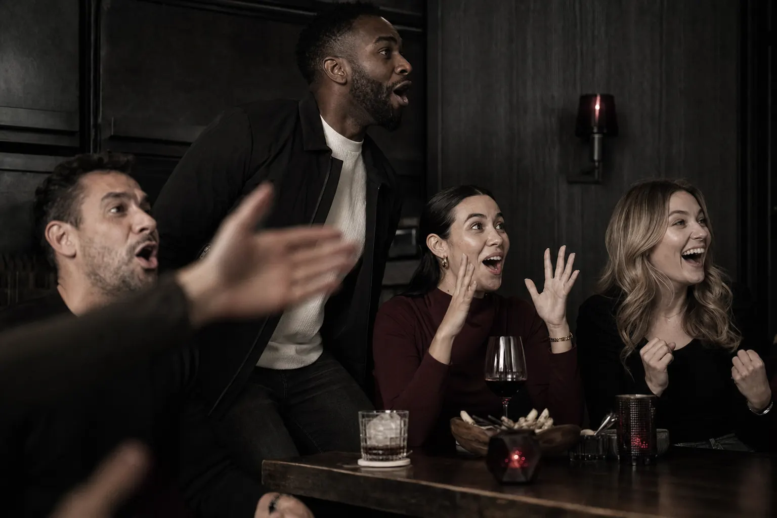 Four friends move and react to a decisive off-camera play in a dark bar.